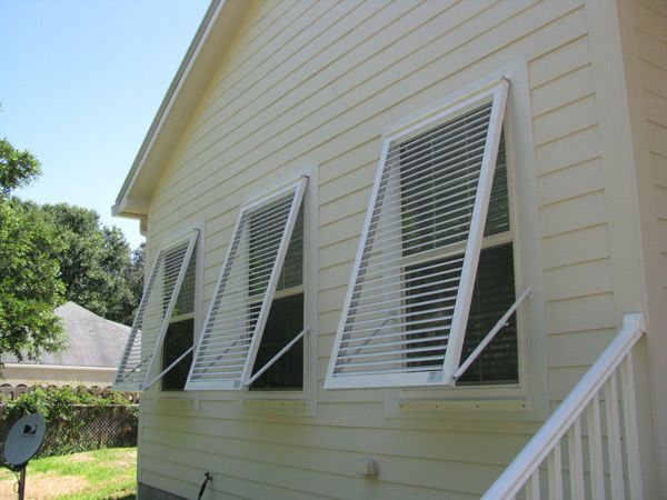 Yellow house with three open, louvered windows. White trim. Sunny outdoor setting.
