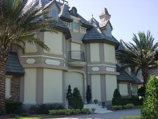 Ornate beige house with closed light-colored shutters; palm trees frame the exterior.