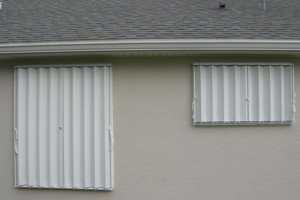 White accordion hurricane shutters on a beige house, protecting windows.