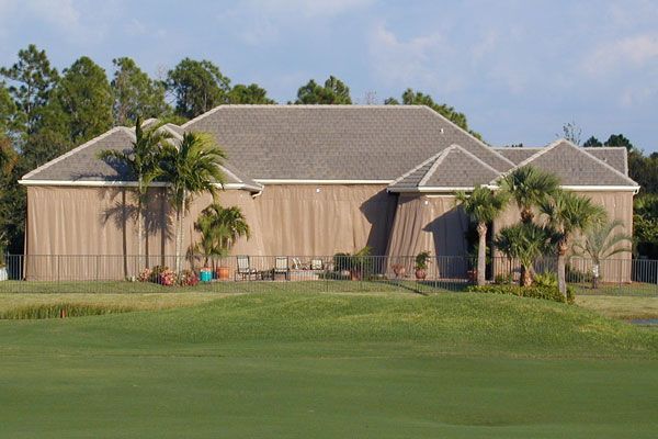 Tan wooden house with gray roof, palm trees, and green lawn.