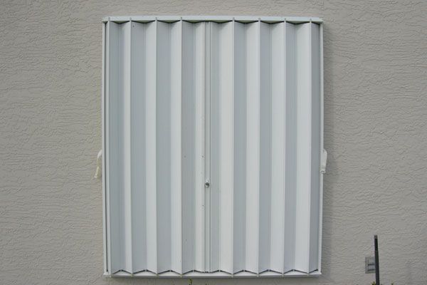 Closed, white accordion-style shutter on a light-colored building exterior.