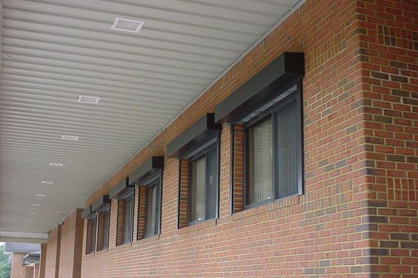 Row of windows with closed black rolling shutters on a brick building with a covered walkway.