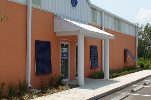 Orange building with white trim, blue shutters, and entrance under a small awning.