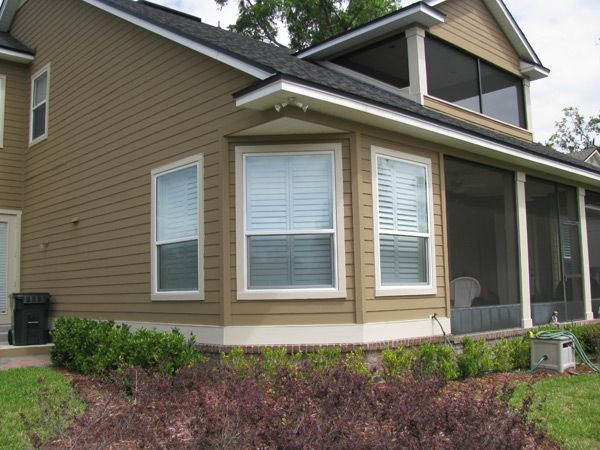 Beige house exterior with windows, attached screened porch, and landscaped garden.