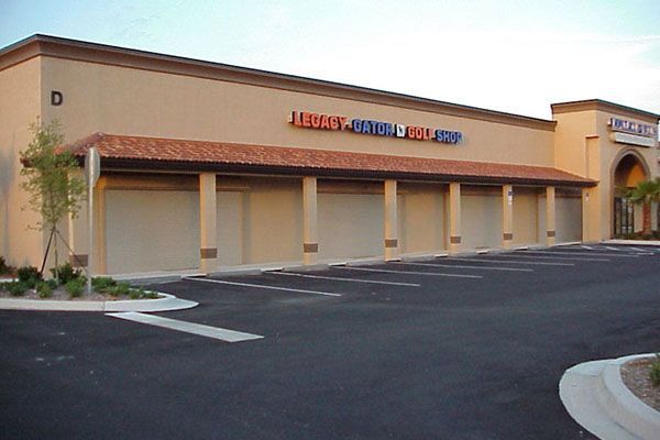 Tan strip mall with closed security shutters, empty parking lot. 