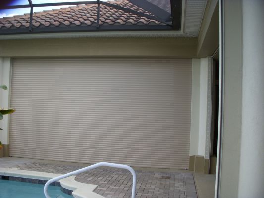 Tan roll-down shutters covering a patio opening next to a pool.