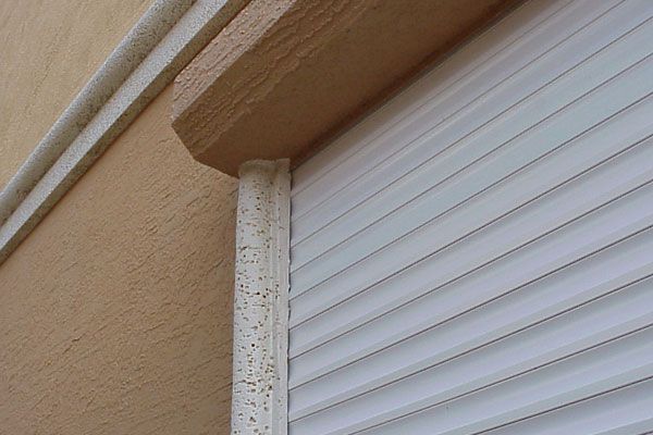 Beige building corner with white window shutters and decorative trim.