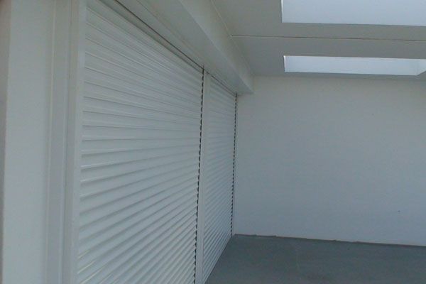 White corrugated blinds covering a wall. A white ceiling with recessed lights is visible.