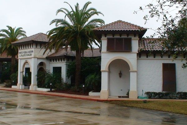 Spanish-style building with white walls, red-tile roof, and palm trees. Cloudy, wet day.