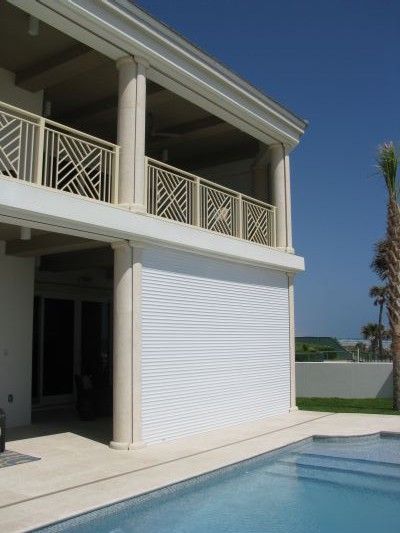 White house with pool, balcony, and closed white shutters.