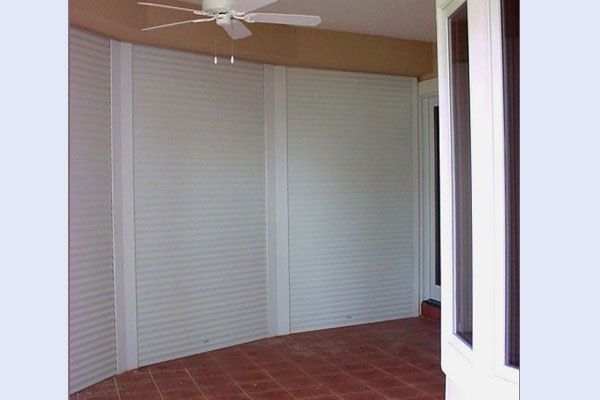 White shuttered outdoor space with curved brick floor and ceiling fan.