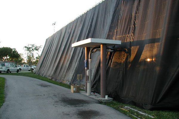 Dark cloth covers a wall; a covered, concrete walkway extends along the left. Brown poles support a small overhang.