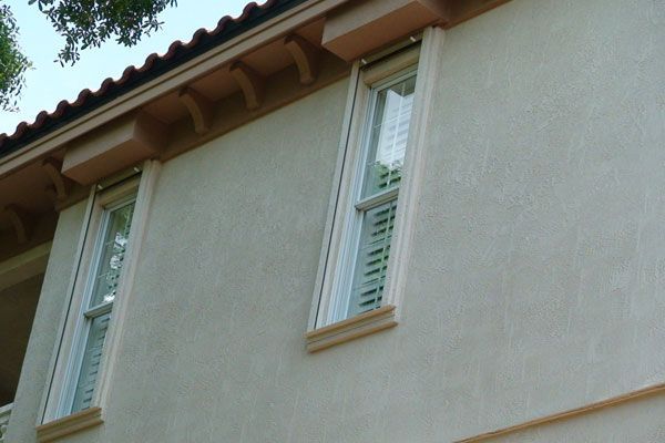 Tan stucco building with two vertical windows, tan trim, and a terracotta tile roof.