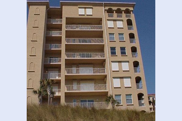 Tan multi-story condominium building with balconies and arched details, blue sky.