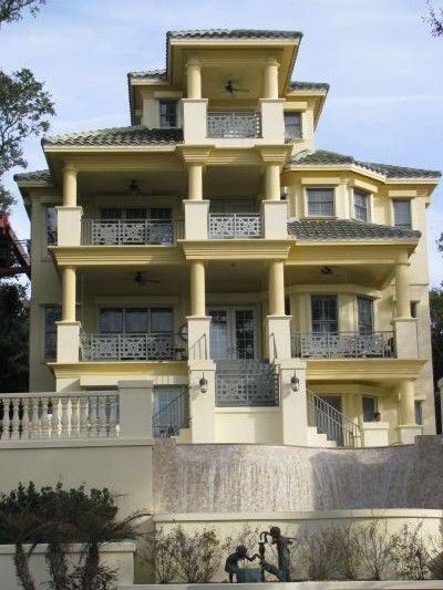 Multi-story beige mansion with balconies, pillars, and a fountain in front.