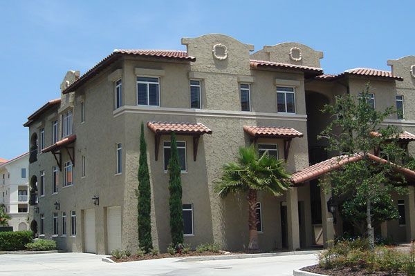 Beige stucco multi-story building with red tile roof, palm tree, and blue sky.