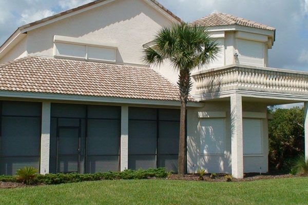 A light-colored house with a screened porch and palm tree in front, on a sunny day.
