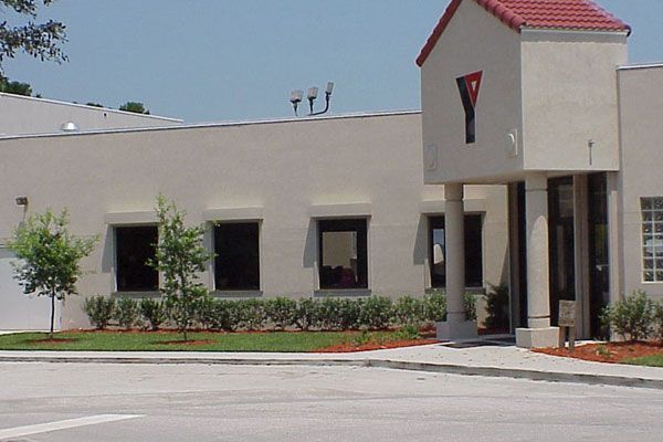 YMCA building with a red roof, cream-colored walls, and small trees and shrubs in front.