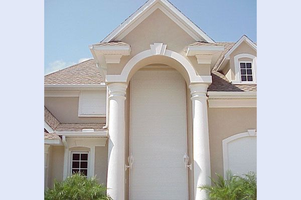 Beige house facade with large arch, white columns, and windows; blue sky.