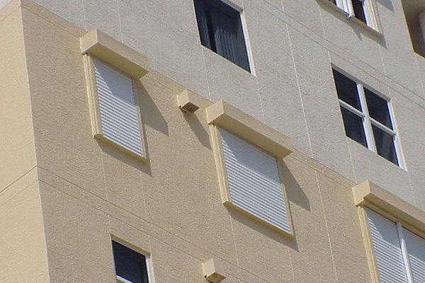 Beige and white building with closed security shutters over some windows.