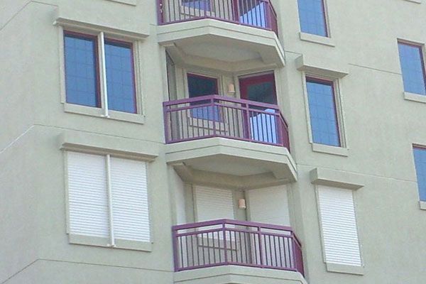 Building exterior with windows, balconies, and cream-colored walls. Purple balcony railings.