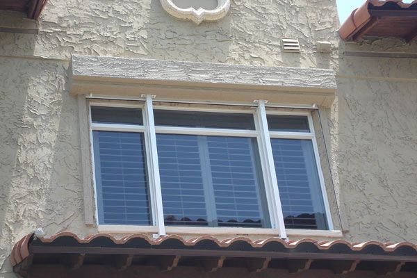 Window with white frame, shuttered glass, and stone trim on stucco building exterior.