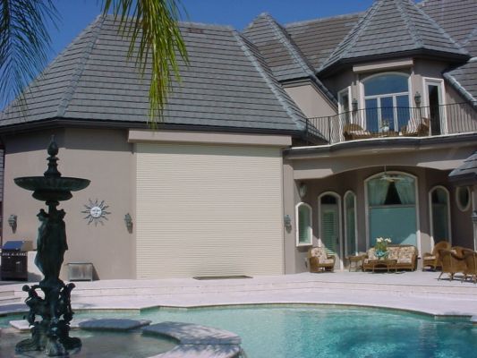 Backyard view of a luxury house with a pool, patio, and fountain, in sunny weather.