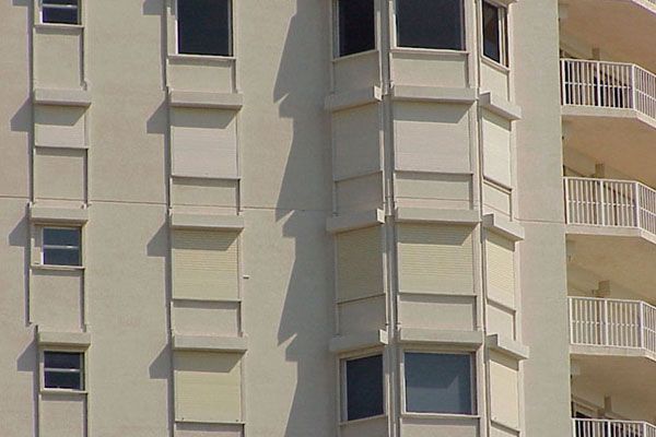 Exterior of a beige high-rise building with windows and balcony railings; sunlight and shadows.