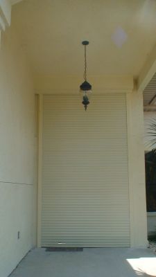 Closed cream-colored rolling shutter on a porch, beneath a light fixture.