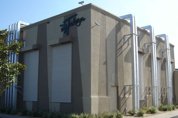 Tan building with a dark logo, vertical tan stripes, and large silver pipes running along the side.