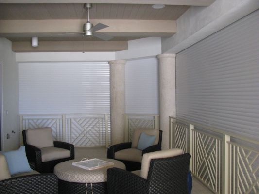 Patio with seating, cream-colored columns, and light-colored shades. Neutral tones, outdoor setting.