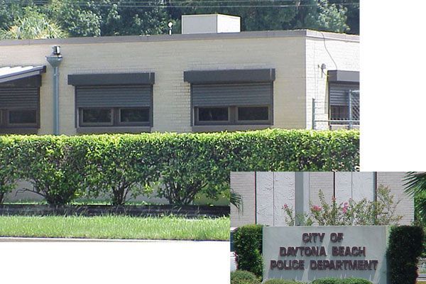 Daytona Beach Police Department building with closed window shutters, green hedges, and sign.