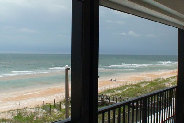 Ocean view from a balcony, beach, waves, overcast sky, sandy shore.