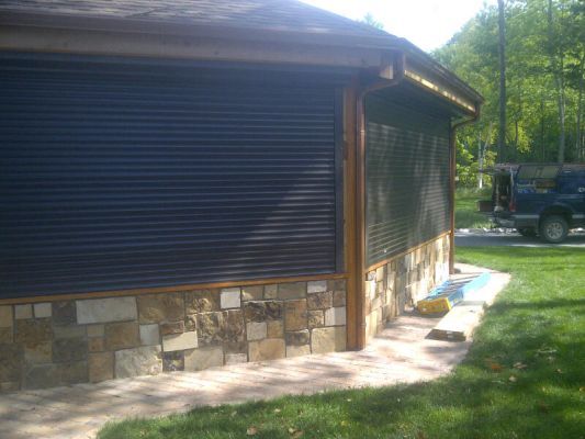 Dark, closed security shutters on a building with stone siding and brick pathway.