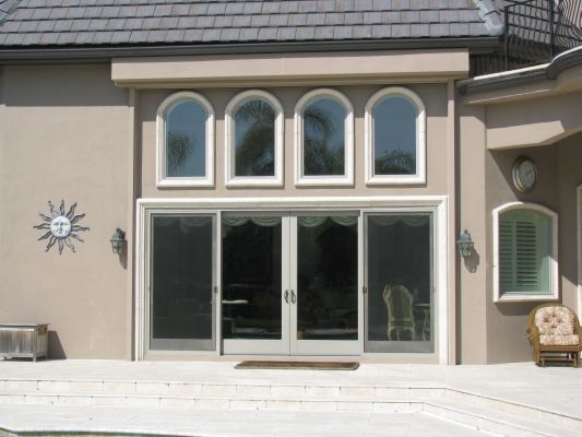 Beige stucco house with arched windows above sliding glass doors, outdoor patio.