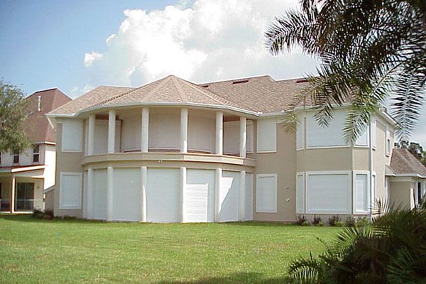 Two-story beige house with white shutters covering the windows and doors.