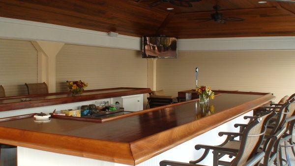 Outdoor bar with wooden counter and stools, TV, and flowers on the bar.