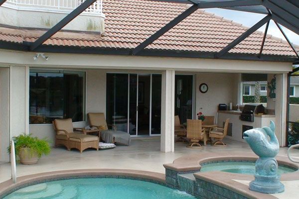 Patio with pool, seating, and built-in grill under a screened enclosure.