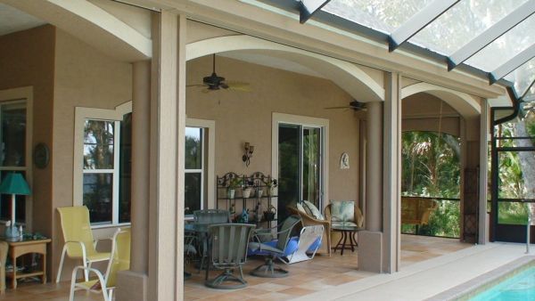 Beige patio with arched columns, windows, and outdoor furniture. A pool is visible to the right.