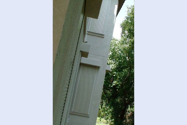 Exterior wall of a building with two shuttered windows and trees.