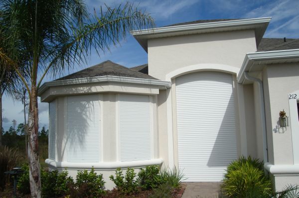 A house with white shutters closed over windows for storm protection. Sunny day.