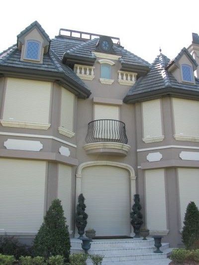 Beige stucco house with roll-down shutters, balcony, and ornate trim.