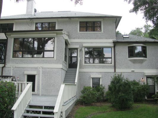Back of a two-story light gray house with large windows, a deck, and stairs leading to a doorway.