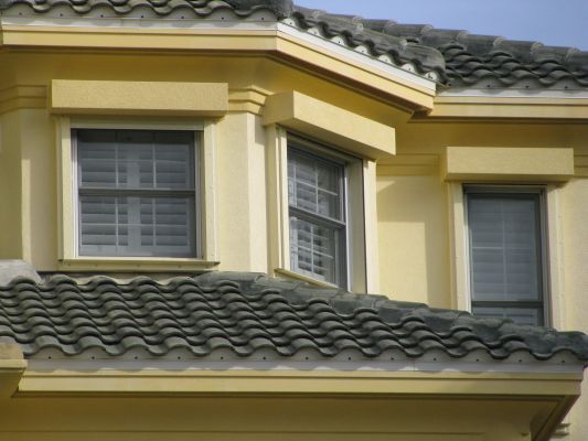 Yellow house with three windows and grey tile roof.