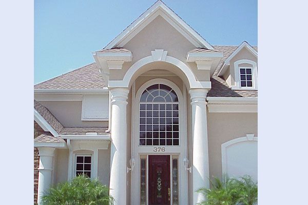 Beige stucco home with columns flanking arched window and door.