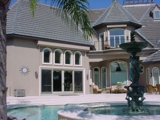 Elegant beige mansion with a pool, fountain, and palm tree.