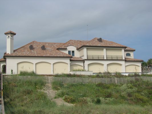 Large white house with orange tile roof, beige hurricane shutters, and sand dunes in front.