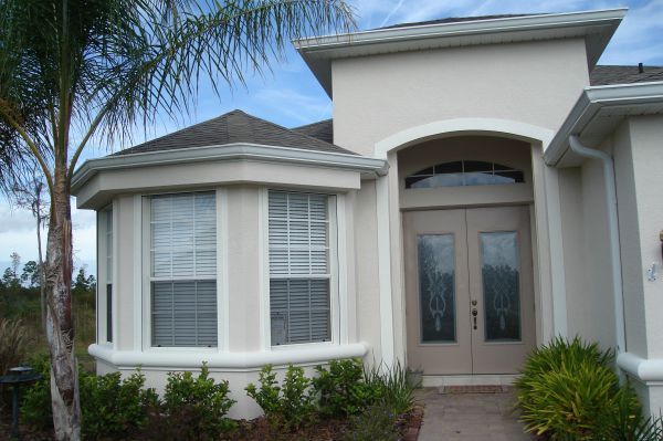 A light-colored house with arched doorway and bay window; palm tree in front.