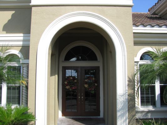 Beige arched doorway with double dark wooden doors; two windows on each side.