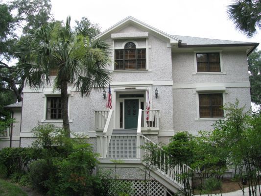 Two-story white house with dark framed windows, porch, and palm tree in front.